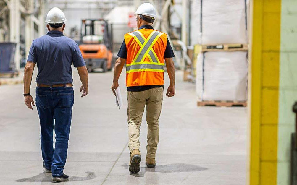 Two people walking into a workplace. Person on left is a workplace representative. Person on the right holding a clipboard is a WorkBright consultant. 